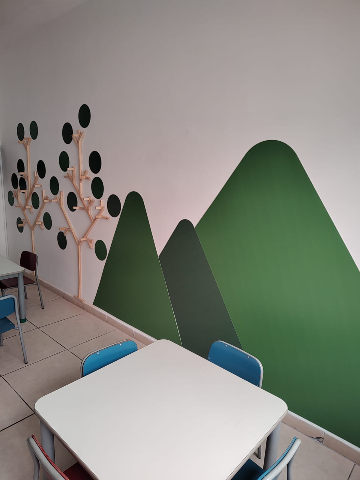 Sala infantil com painel de montanhas verdes e cabideiros em forma de árvore