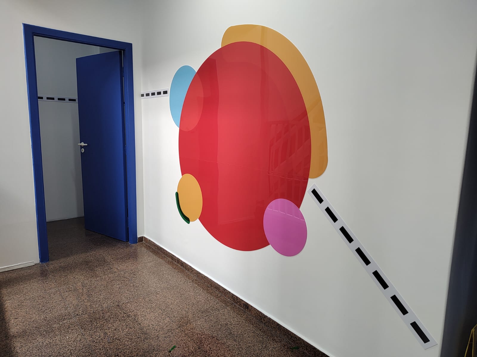 Painel de círculos coloridos aplicado na parede ao lado de porta azul