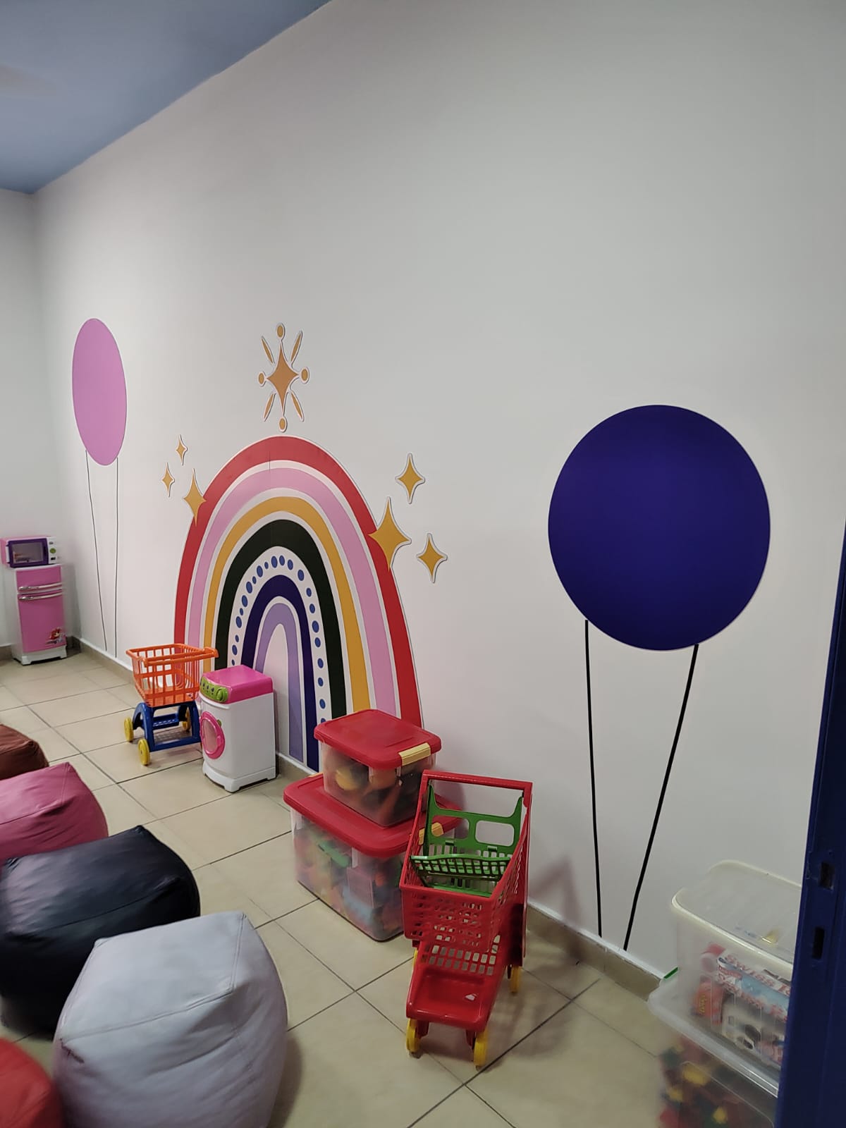 Área infantil com grafismos lúdicos na parede: arco-íris colorido, balões e estrelas aplicados