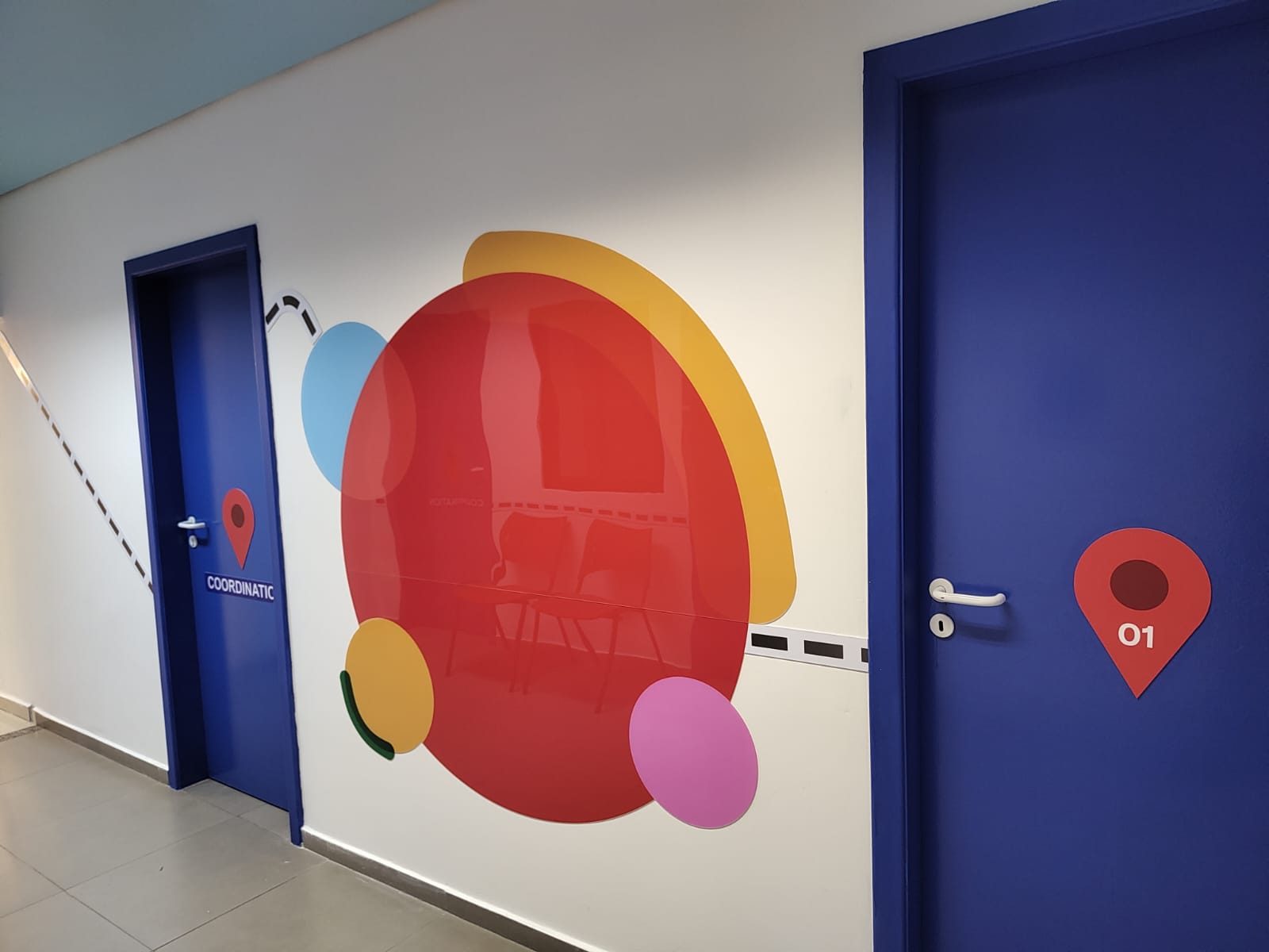 Corredor com grande painel de círculos coloridos entre a porta da coordenação e a sala 01