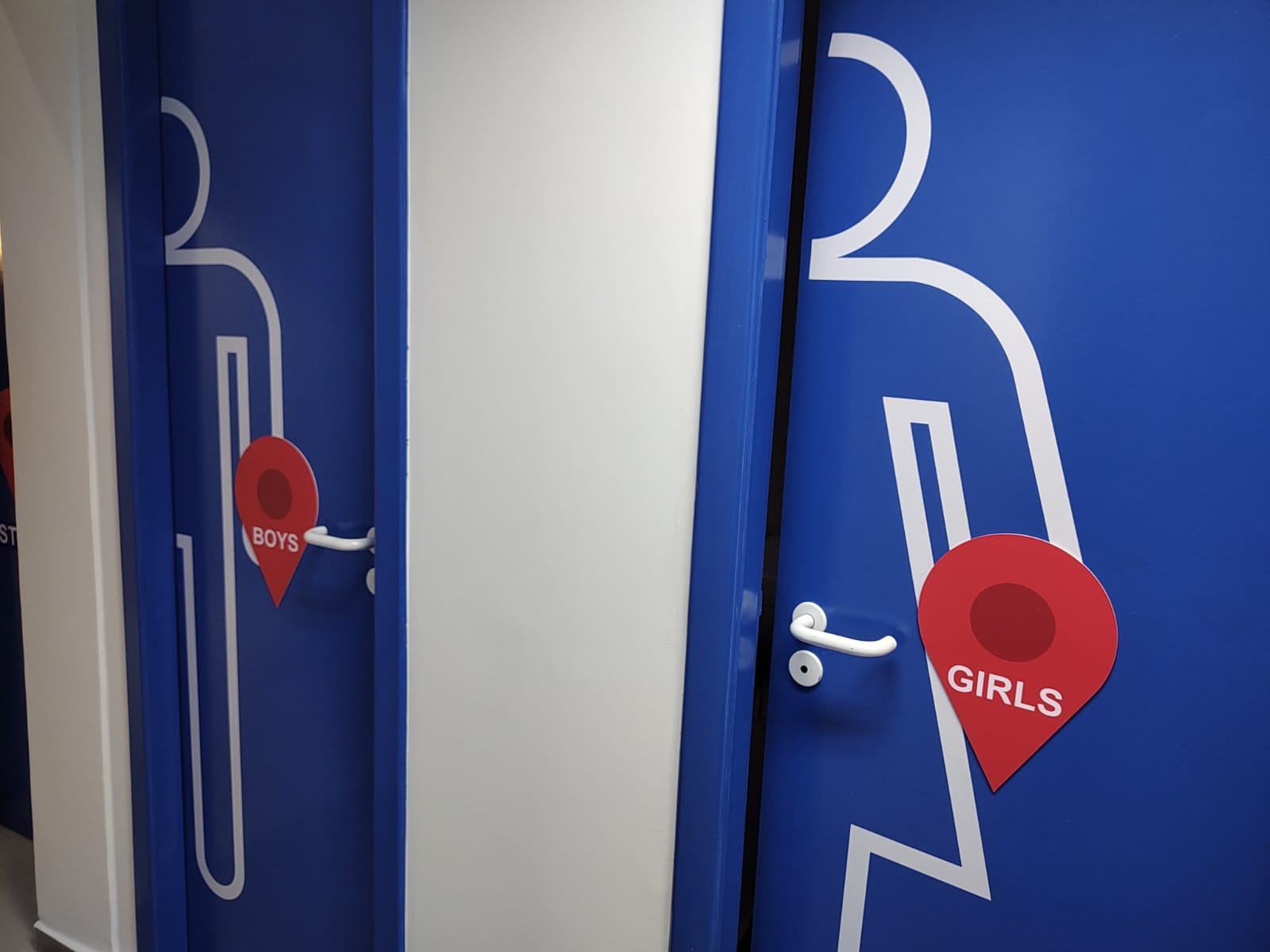 Portas azuis dos banheiros com pictogramas brancos e marcadores vermelhos Boys e Girls